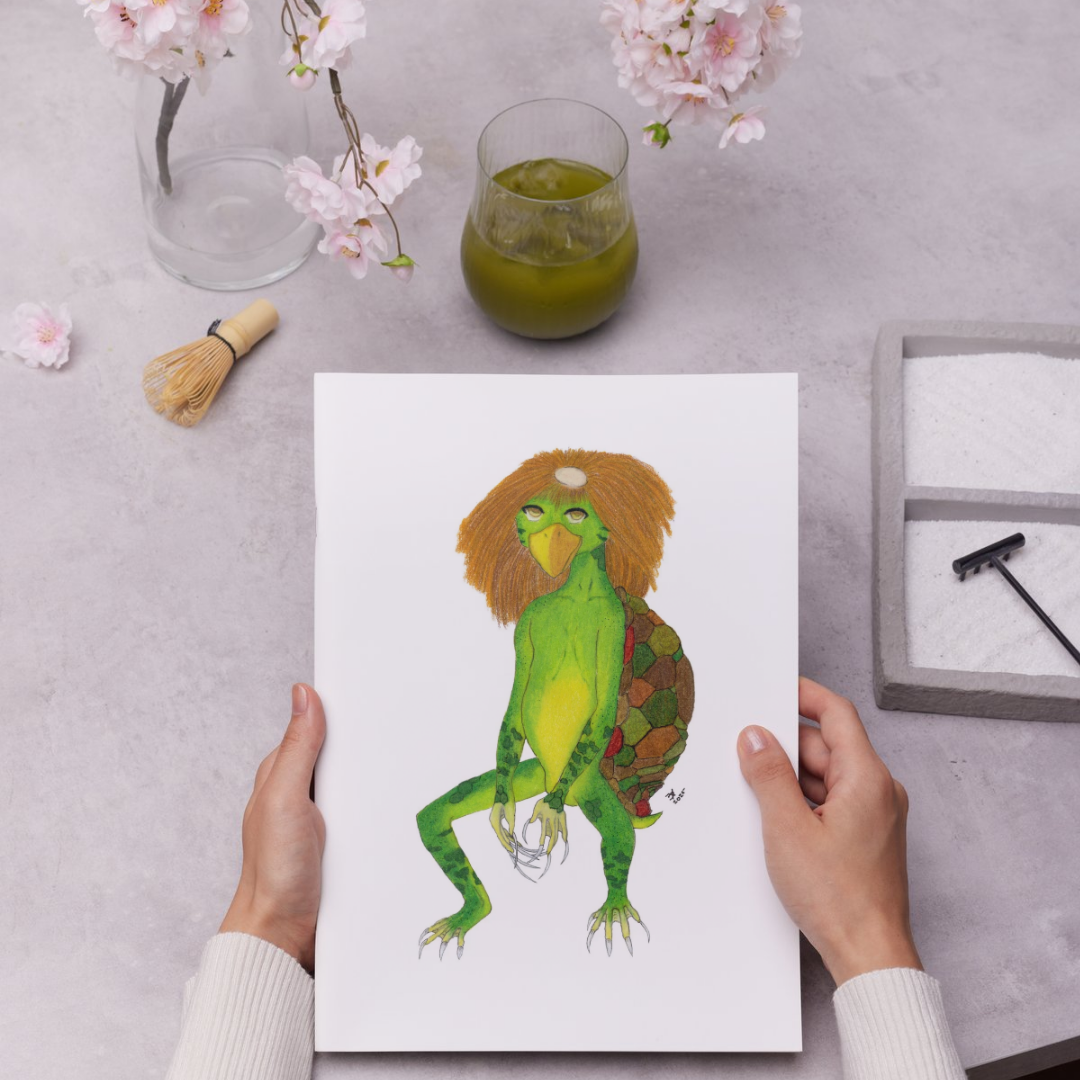 Person holding a card with a colorful illustration of a kappa creature on a table with a glass of green liquid and flowers.